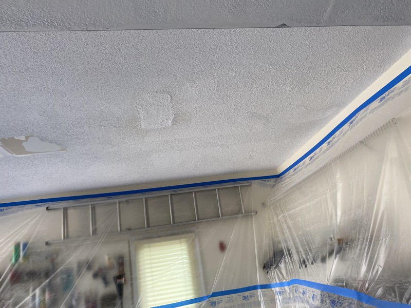 Popcorn ceiling patched with the room masked in plastic for finishing