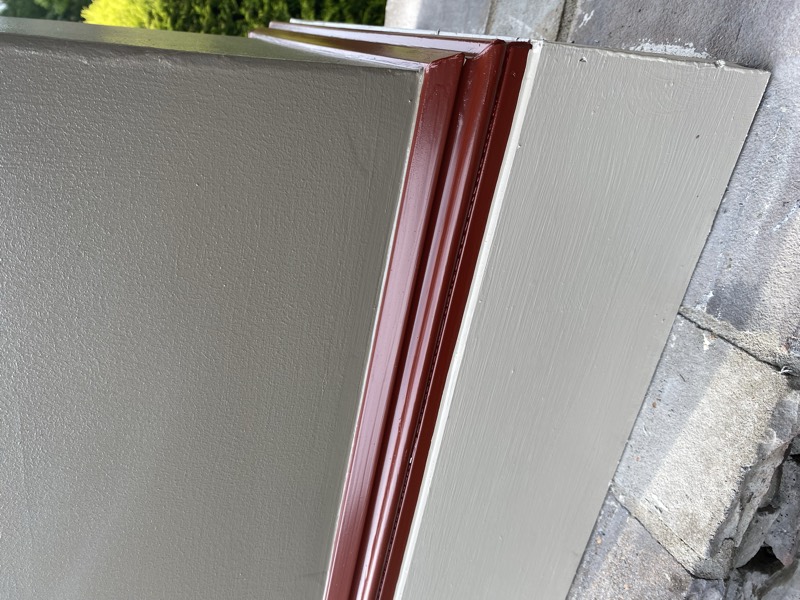 Freshly painted exterior wall with red accent trim over stone