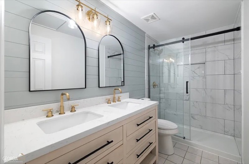 Renovated bathroom with a double vanity, arched mirrors, and marble-tile shower