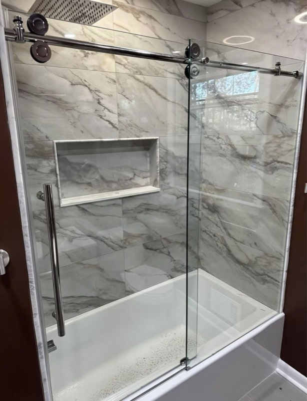 Bathtub with a marble-look tile surround and frameless sliding glass